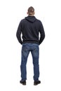 A young man in a hoodie and jeans stands with his back to the camera. Back view. Full height. Isolated over white background. Royalty Free Stock Photo