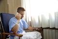 Young man at hospital room wearing patient pajamas sitting by the window talking on mobile phone Royalty Free Stock Photo