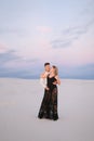 Young man hugging blonde woman wearing black dress and standing in snowed field. Royalty Free Stock Photo