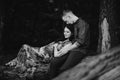 Young man hugs his pregnant wife, sitting on big fallen tree in summer nature Royalty Free Stock Photo