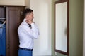 A young man husband is going to a wedding ceremony in a luxury hotel wearing a blue suit and adjusting his bow tie while waiting Royalty Free Stock Photo