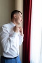 A young man husband is going to a wedding ceremony in a luxury hotel wearing a blue suit and adjusting his bow tie while waiting Royalty Free Stock Photo