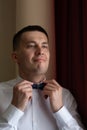 A young man husband is going to a wedding ceremony in a luxury hotel wearing a blue suit and adjusting his bow tie while waiting Royalty Free Stock Photo