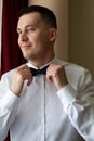 A young man husband is going to a wedding ceremony in a luxury hotel wearing a blue suit and adjusting his bow tie while waiting Royalty Free Stock Photo