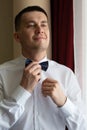 A young man husband is going to a wedding ceremony in a luxury hotel wearing a blue suit and adjusting his bow tie while waiting Royalty Free Stock Photo