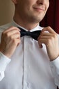 A young man husband is going to a wedding ceremony in a luxury hotel wearing a blue suit and adjusting his bow tie while waiting Royalty Free Stock Photo