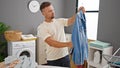 Young man ironing clothes with steam vertical ironing machine at laundry room