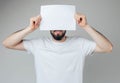 Young man isolated over background. Bearded guy cover part of face with white blank page. Hold it with both hands