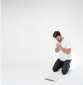 Young man isolated over background. Guy stand on knees and pray in front Bible. Studying word of God. Believe or faith