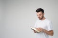 Young man isolated over background. Side view of guy reading book and standing in room alone. Point with finger. Smart