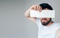 Young man isolated over background. Side view and selfie of bearded guy hide eyes from camera. Hold iece of paper or