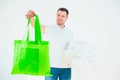 Young man isolated over white background. Guy hold green eco bag in one hand and planty white plastic bags in another Royalty Free Stock Photo