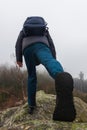 Young man in jacket and with backpack walking on rock in fog misty morning. Explore, alone trip background, bottom angle Royalty Free Stock Photo