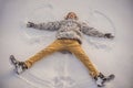 A young man in jacket lies on the snow and makes the figure of an angel. Winter fun