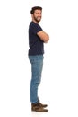 Young Man In Jeans And Blue T-shirt Is Standing With Arms Crossed. Side View Royalty Free Stock Photo