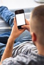 Young man in jeans looking at smartphone screen sitting on sofa at home Royalty Free Stock Photo