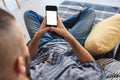 Young man in jeans looking at smartphone screen sitting on sofa at home Royalty Free Stock Photo