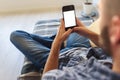 Young man in jeans looking at smartphone screen sitting on sofa at home Royalty Free Stock Photo