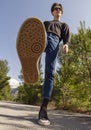 A young man in jeans and sneakers goes on the road among the trees