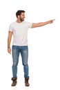 Young Man In Jeans And White T-shirt Is Standing, Pointing At The Side And Looking Away. Front View Royalty Free Stock Photo