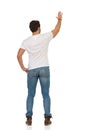 Young Man In Jeans And White T-shirt Is Standing And Waving Hand. Rear View