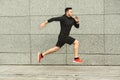 Young man jogging in city against grey urban wall, copy space, side view Royalty Free Stock Photo