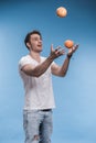 Young man juggling with fruits on blue