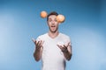 Young man juggling with fruits on blue