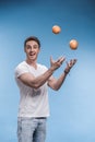 Young man juggling with fruits on blue