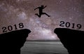 A young man jump between 2018 and 2019 years over night sky with stars and through on the gap of hill silhouette evening colorful