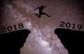 A young man jump between 2018 and 2019 years over night sky with stars and through on the gap of hill silhouette evening colorful