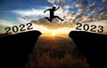 A young man jump between 2022 and 2023 years over the sun and through on the gap of hill  silhouette evening colorful sky. happy n Royalty Free Stock Photo