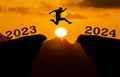 A young man jump between 2023 and 2024 years over the sun and through on the gap of hill silhouette evening colorful sky. happy ne Royalty Free Stock Photo