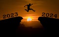 A young man jump between 2023 and 2024 years over the sun and through on the gap of hill silhouette evening colorful sky. happy ne Royalty Free Stock Photo