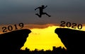 A young man jump between 2019 and 2020 years over the sun and through on the gap of hill silhouette evening colorful sky.
