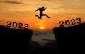 A young man jump between 2022 and 2023 years over the sun and through on the gap of hill  silhouette evening colorful sky. Royalty Free Stock Photo