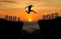 A young man jump between 2021 and 2022 years over the sun and through on the gap of hill  silhouette evening colorful sky. Royalty Free Stock Photo