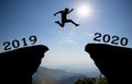 A young man jump between 2019 and 2020 years over the sun and through on the gap of hill silhouette evening colorful sky.