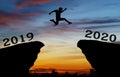 A young man jump between 2019 and 2020 years over the sun and through on the gap of hill silhouette evening colorful sky. Royalty Free Stock Photo