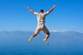 Young man jumping on rock with his hands up blue ocean mountain peaks horizon. Active holiday adventure, tourism action, healthy Royalty Free Stock Photo