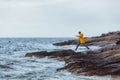young man jumping at rocky sea coast in yellow raincoat in storm weather