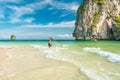 Young man jumps in the shallow sea waters with a large limestone cliff covered with tropical vegetation