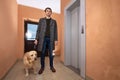 Young man with labrador dog in coat standing in hallway and waiting elevator Royalty Free Stock Photo
