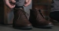 Young man lace up his brown leather chukka boots indoor