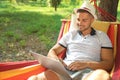 Young man with laptop resting in comfortable hammock at garden Royalty Free Stock Photo