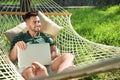 Young man with laptop resting in comfortable hammock at garden Royalty Free Stock Photo