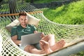 Young man with laptop resting in comfortable hammock at garden Royalty Free Stock Photo