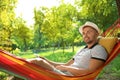 Young man with laptop resting in hammock at green garden Royalty Free Stock Photo