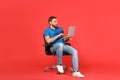 Young man with laptop sitting in comfortable office chair on red background Royalty Free Stock Photo