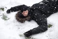 Young man laughing, with happy expression, snow covered, lying on the ground in snowfall. Royalty Free Stock Photo